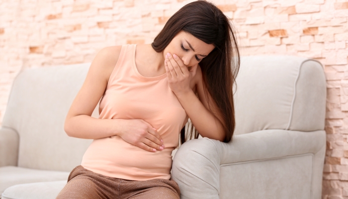 Beautiful pregnant woman suffering from nausea sitting on couch.