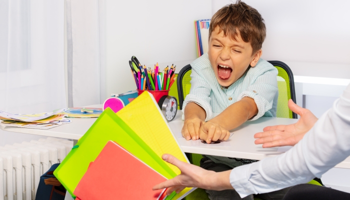 Boy with autism spectrum disorder throw textbooks and books from table in negative expression behavior sitting near teacher.