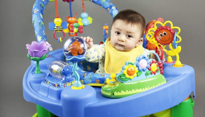 Cute multi-racial asian caucasian baby boy in yellow bib playing in colorful exersaucer.