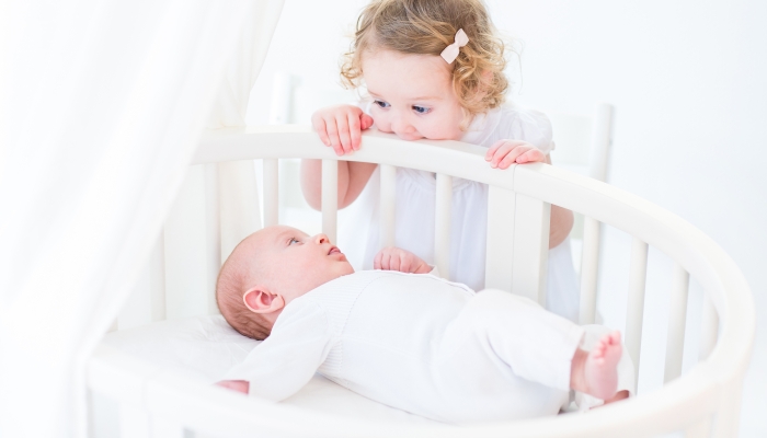 Cute newborn baby boy watching his toddler sister laying in a bassinet.