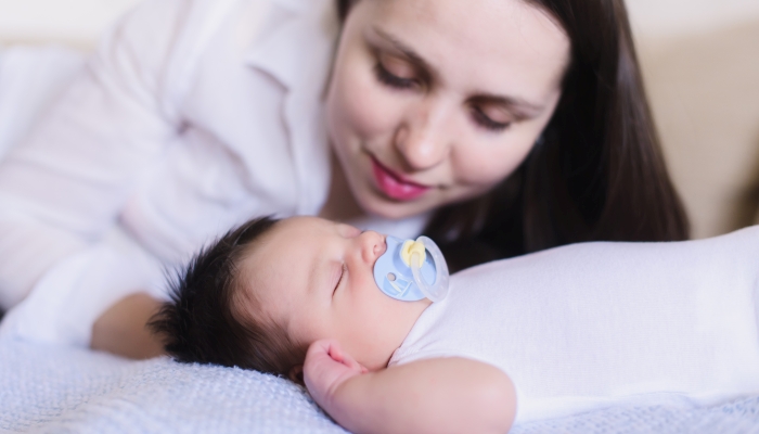 Happy young mother near sleeping baby with pacifier.