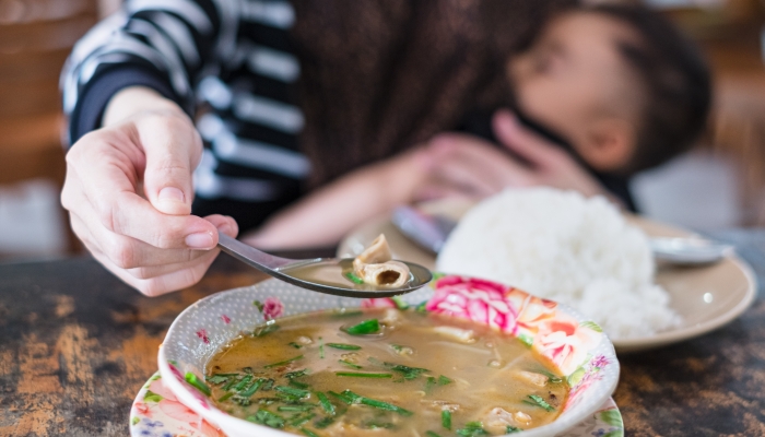 Hungry mother is eating lunch with variety of food menu while breastfeeding baby at restaurant.