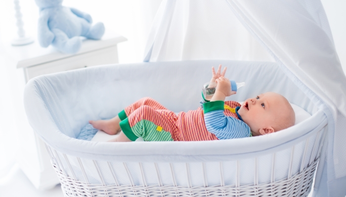 Little baby with bottle in white bassinet.