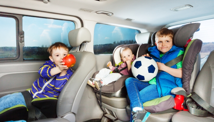 Three little boys, age-diverse brothers, travelling by car in safety seats, snacking and playing ball during the trip.