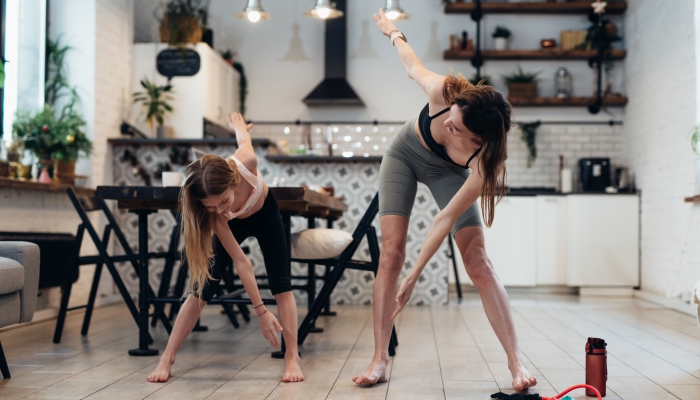 Mother and daughter do sports at home, do standing bends to their toes, twisting their backs.