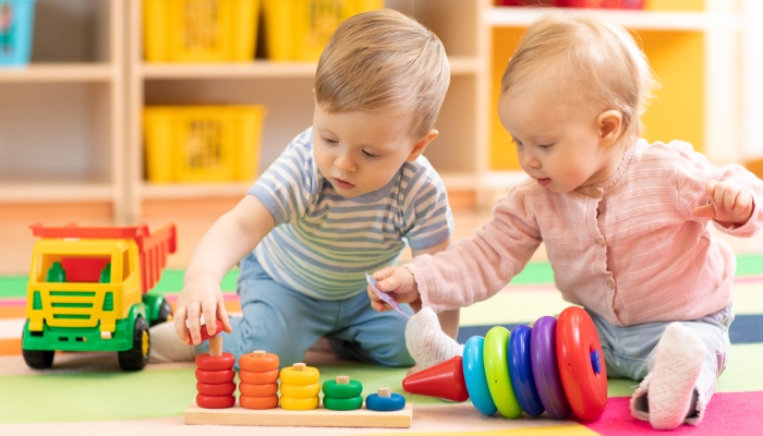 Preschool boy and girl playing on floor with educational block toys.