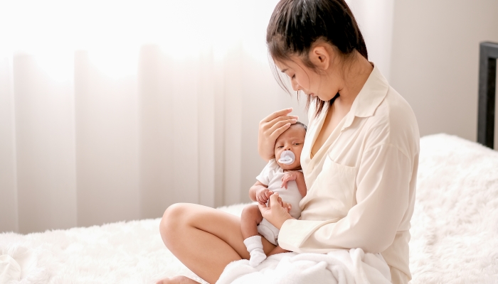 Soft blur image of beautiful Asian mother hold her newborn baby with baby teat on the white bed.