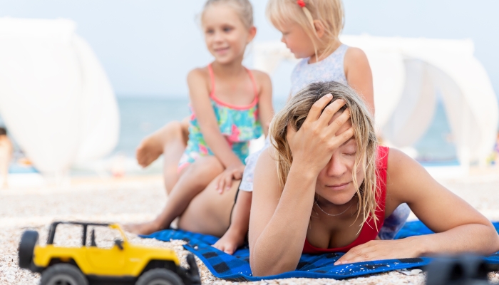 Two cute little sibling girls enjoy having fun playing sitting on tired exhausted mothers back at sea ocean beach.