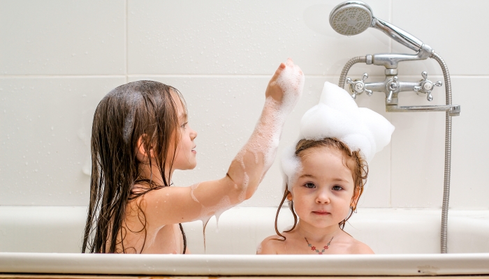 Two little sisters play in a bath.