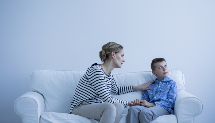 Protective woman comforting a young, autistic boy in a white room.