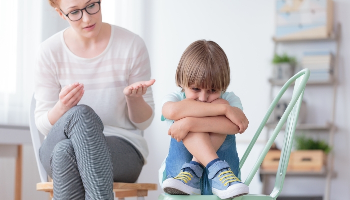 Worried autistic boy sitting with crossed legs on mint chair during conversation with psychiatrist.