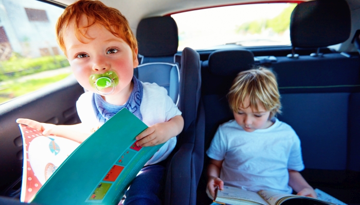 Young kids sitting on back seat, reading book while traveling in the car.