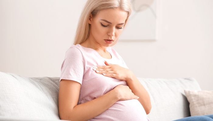 Young pregnant woman touching her breast at home.