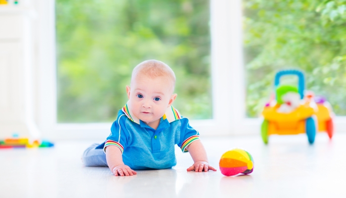 Adorable baby boy playing with a colorful ball and toy car during a tummy time.