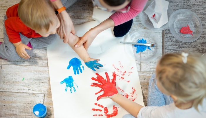 Adorable cute caucasian little blond siblings children enjoy having fun together with mother painting brush and palm at home indoors.