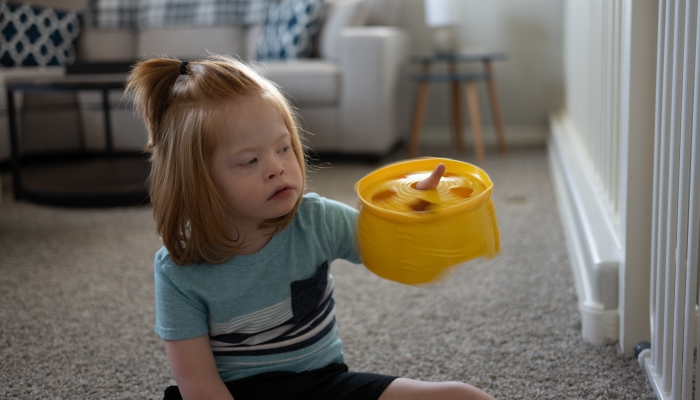 Boy with Down syndrome, with long hair and ponytail, spinning an out of focus yellow toy on his finger.
