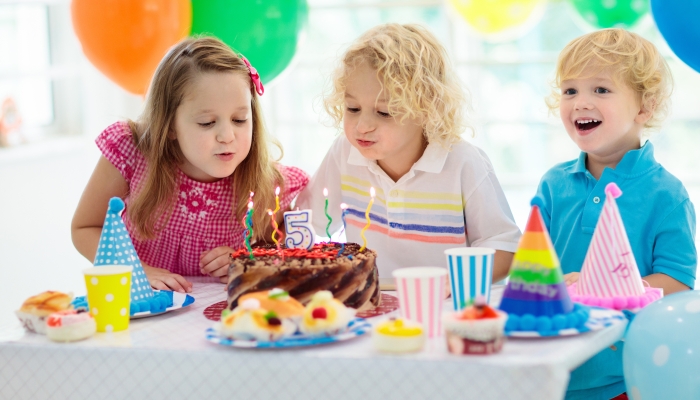 Child blowing out candles on colorful cake.
