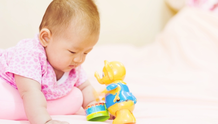 Cute adorable newborn baby playing on colorful toy in a tummy time.