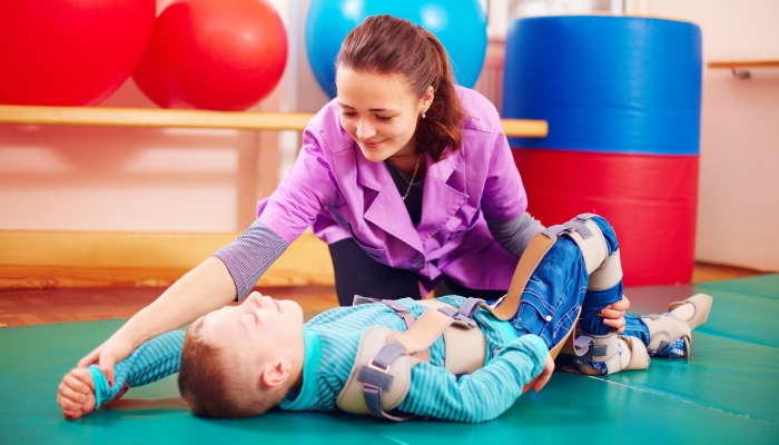 Cute kid with disability has musculoskeletal therapy by doing exercises in body fixing belts.