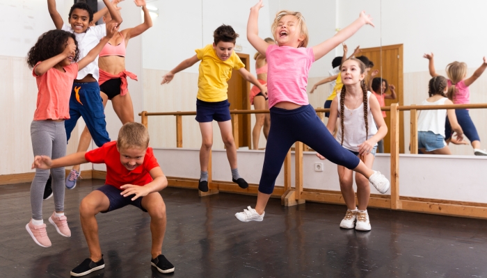 Group of happy sporty kids with female teacher training in modern dance studio, jumping together.