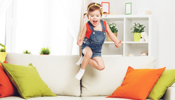 Happy child girl playing and jumping on couch at home.