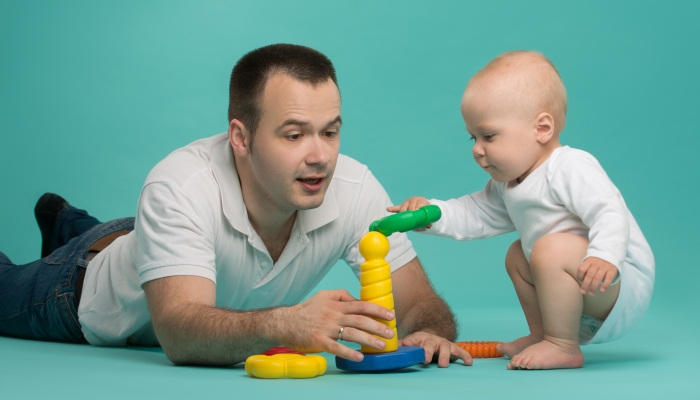 Happy handsome smiling Caucasian father playing with his son baby boy, picking up pyramid circles.