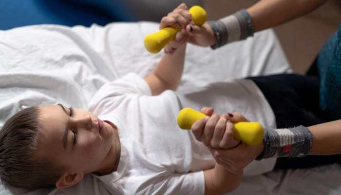 Little boy with cerebral palsy has musculoskeletal therapy by doing exercises in body fixing.