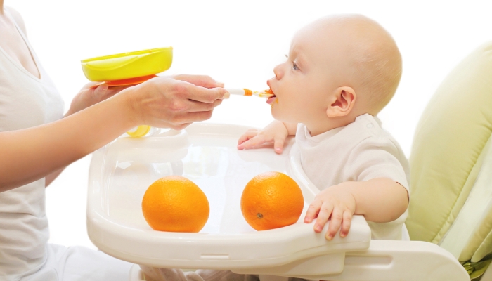 Mother feeds baby spoon on the table home.
