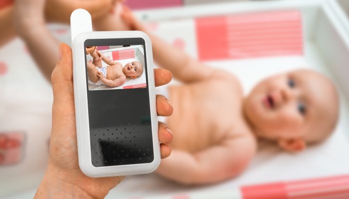 Hand of mother is holding baby monitor camera for safety of her cute baby.