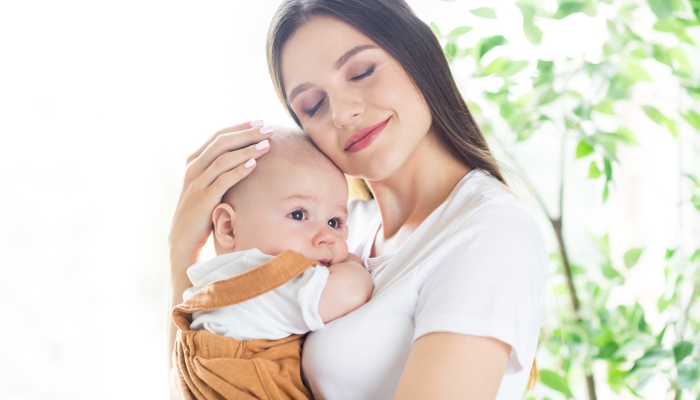 Photo of cheerful relaxed mother pretty lady hold small newborn baby boy cuddle wear white t-shirt home indoors.