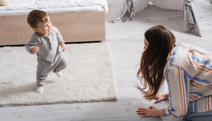 Tattooed young mother encouraging infant son walking first steps.