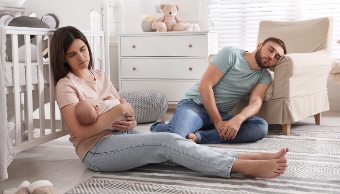 Tired young parents with their baby sleeping on floor in children's room.