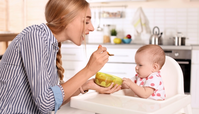 Woman feeding her child in highchair indoors.