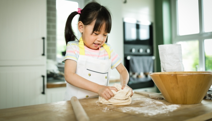 Young girl making bread dough at home kitchen for home schooling.