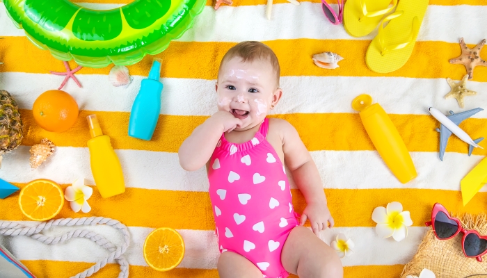A baby girl smears sunscreen on her skin.