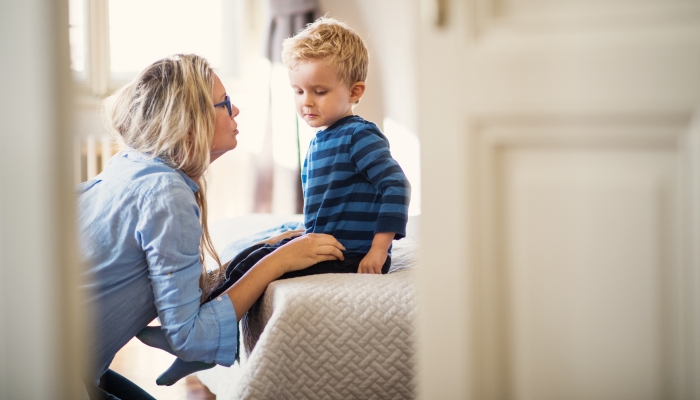 A young mother talking to her toddler son inside in a bedroom.