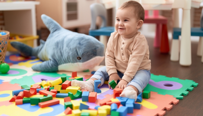 Adorable toddler playing with wooden construction blocks sitting in a playroom.