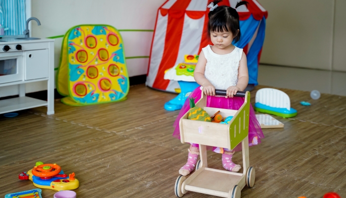 Asian baby girl playing a shopping cart toys in playroom.