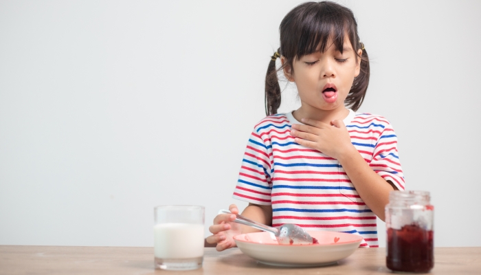 Asian children girls eating bread and desserts and sticking in one's throats with choked food or puke on the table at home for breakfast or lunch