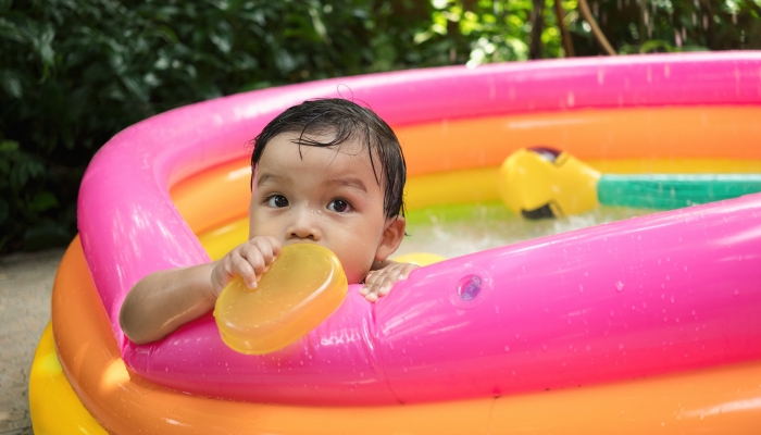 Baby boy play water and bite yellow bowl toy in kiddie pool by alone.