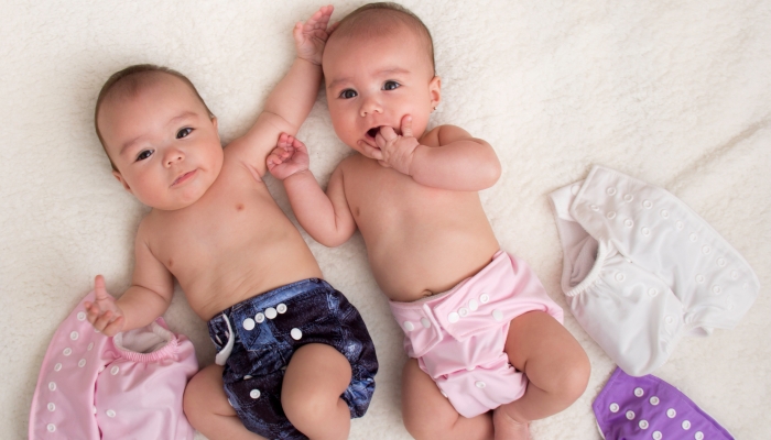 Baby twins girls with cloth diaper on a bed.