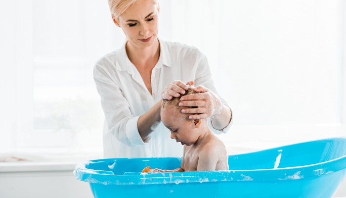 Beautiful blonde mother washing head of toddler son in bathroom.