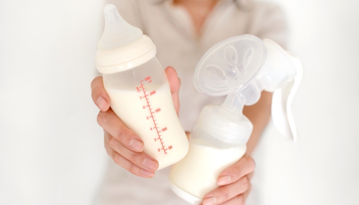Breast pump and bottle with milk in woman's hand.