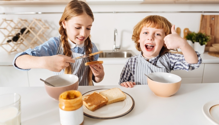 Brilliant bright siblings having fun during breakfast with a peanut butter sandwich.