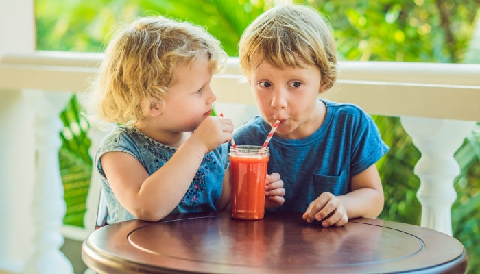 Children boy and girl drink orange smoothie from papaya.