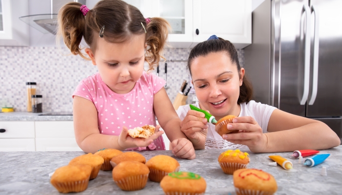 Close-up Of Mother And Daughter Decorating Homemade Cupcake Together In Kitchen.