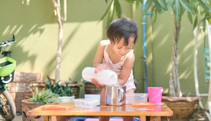 Cute Asian toddler girl child having fun pouring water into cup at home.
