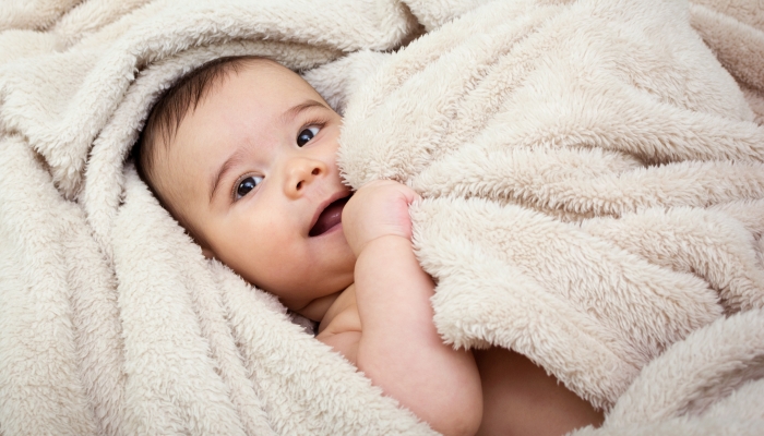 Cute baby boy in bed under a fluffy blanket.