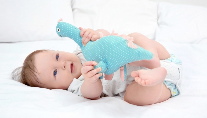 Cute baby playing with toy dinosaur on bed.