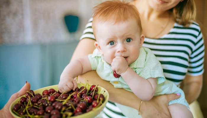 Cute little baby with cherry in hands and mother in summer home.